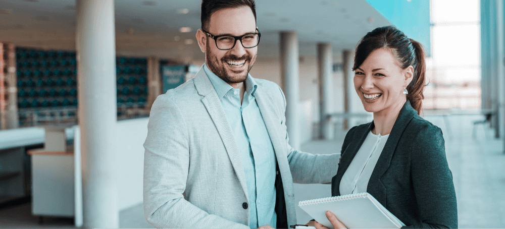 A businessman and businesswoman smiling and standing together holding bill review report sheets