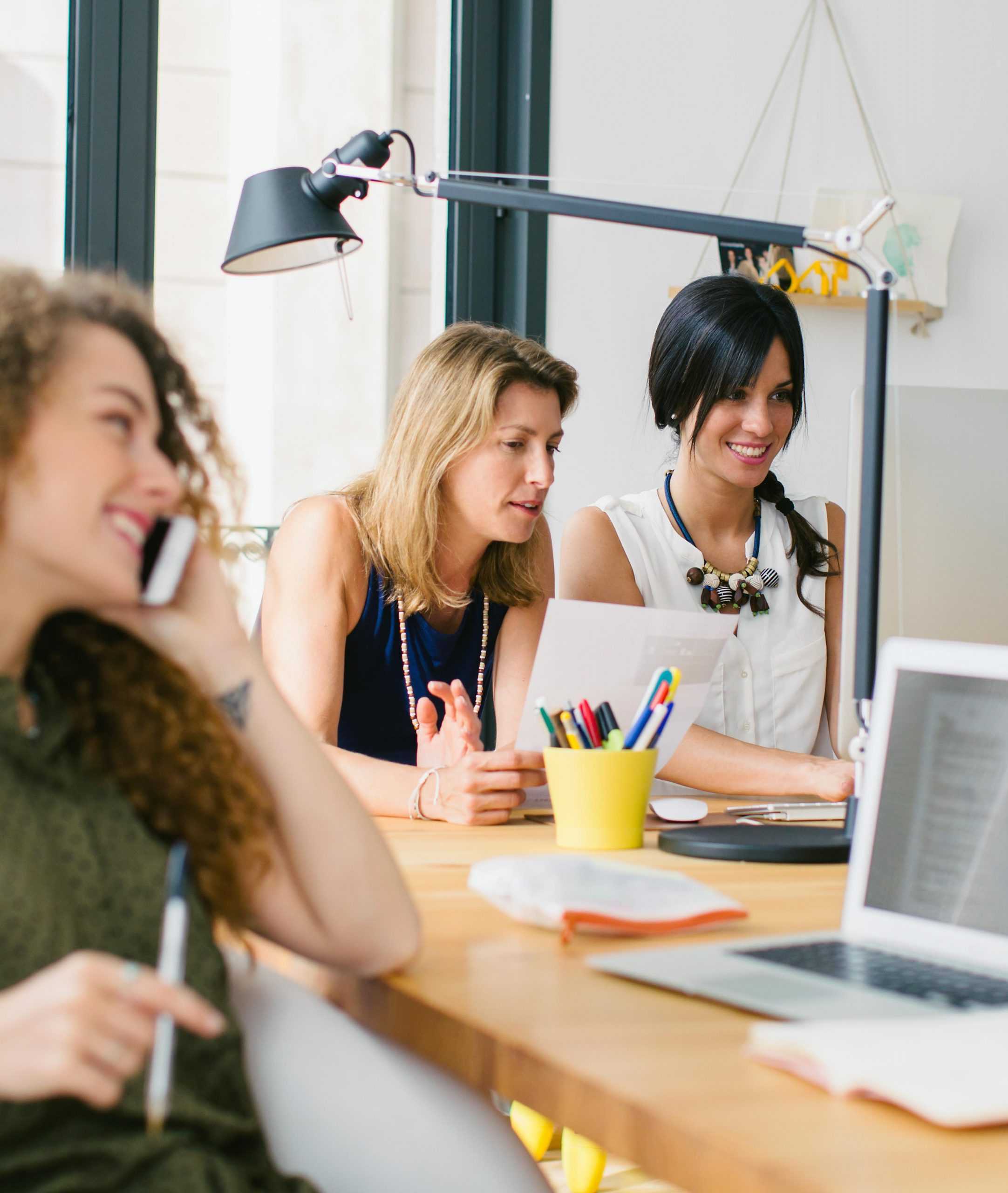 A group of female colleagues working around a desk smiling and enjoy the CERIS company culture.