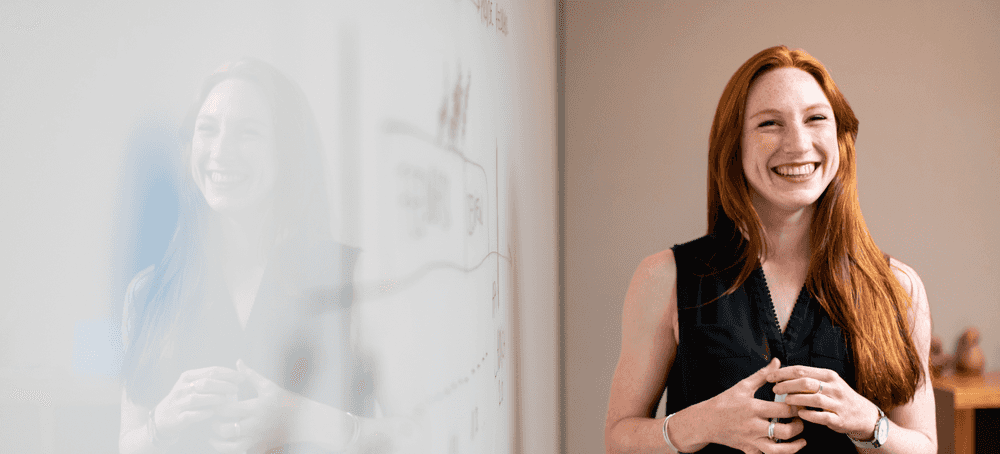 A woman smiling and standing next to a whiteboard with payment integrity notes on it