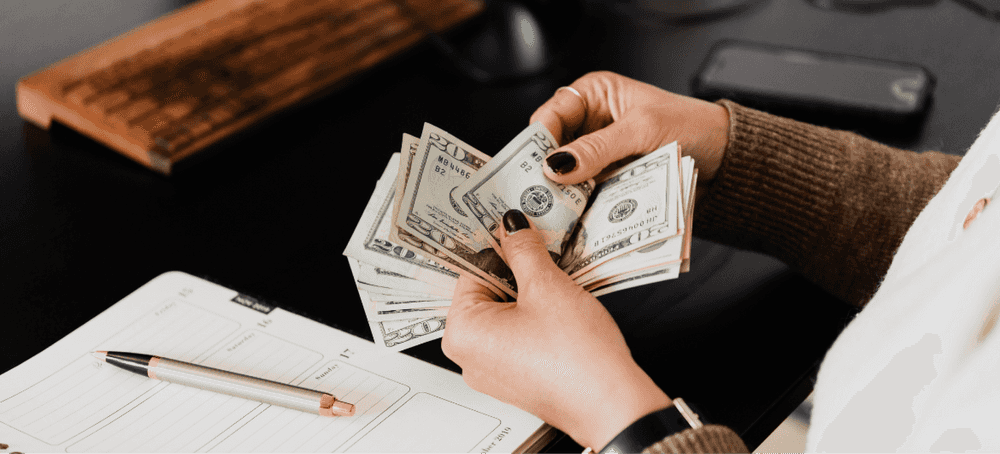 A person counting a stack of dollar bills at their desk